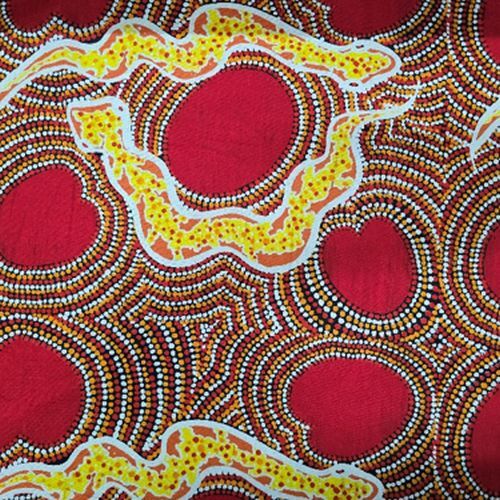 A close-up of a fabric featuring an Aboriginal-style dot painting pattern with red circular and wavy forms, yellow dotted bands, and brown and white dot details.
