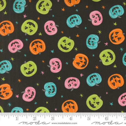 A close-up of fabric with a repeating Halloween pattern of jack-o'-lanterns in orange, pink, green, and teal on a black background, with a ruler along the bottom showing scale and Modas Fabrics branding.