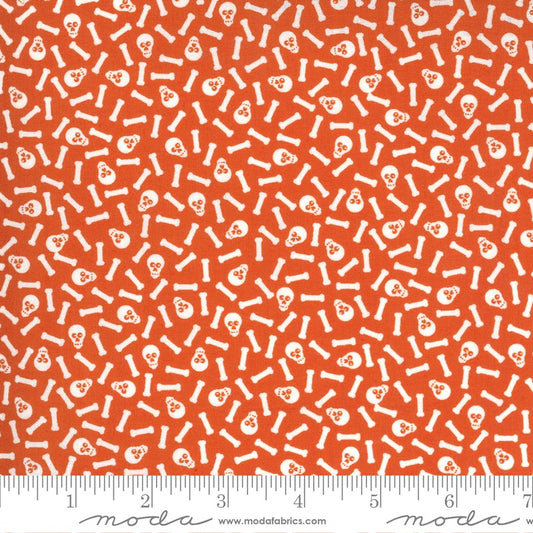 Orange fabric with a repeating white pattern of skulls and bones, shown flat with a measuring ruler along the bottom edge.