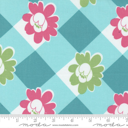 A close-up of a fabric pattern featuring pink and green flowers on a light blue and teal argyle background, with a white ruler along the bottom edge showing the scale.