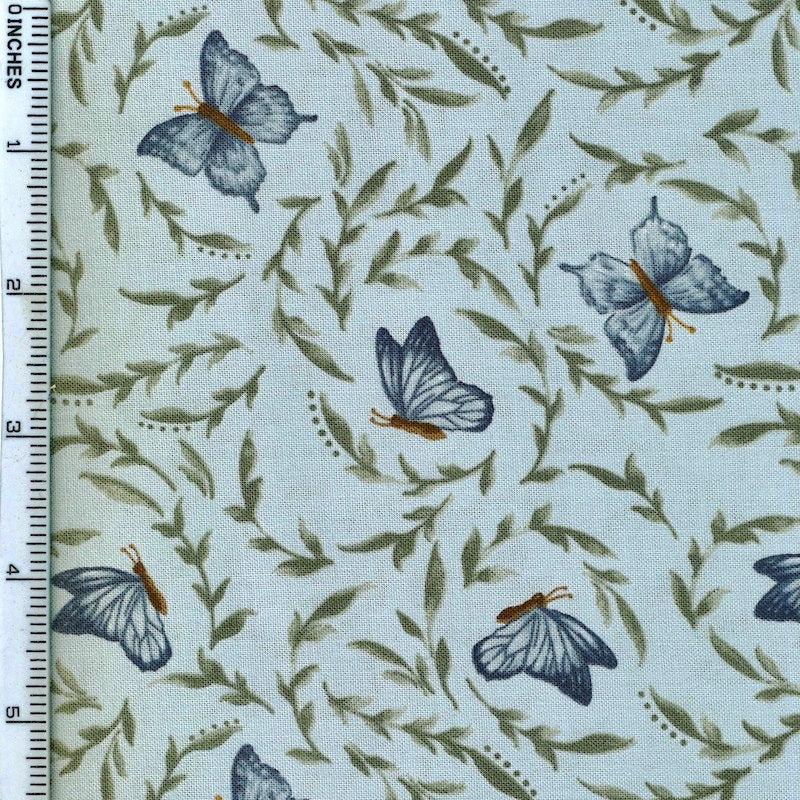 A close-up of a fabric pattern featuring blue butterflies and olive green leaves on a pale blue background, with a white ruler along the left edge showing measurements.