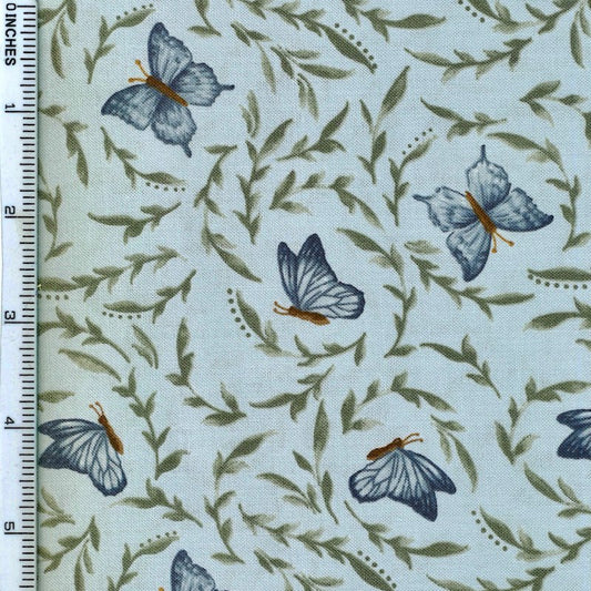 A close-up of a fabric pattern featuring blue butterflies and olive green leaves on a pale blue background, with a white ruler along the left edge showing measurements.