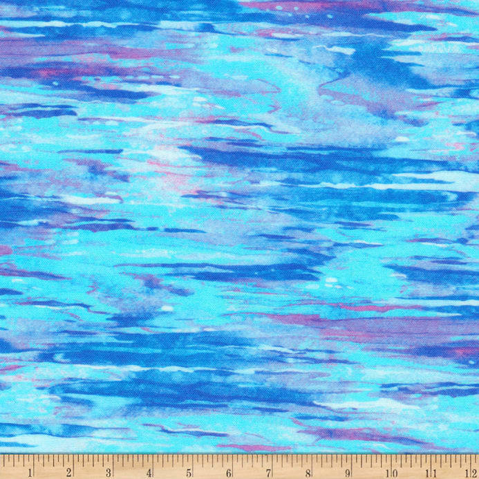 A close-up of a fabric with an abstract watercolor-like pattern in bright cyan, blue, purple, and pink, with a wooden ruler along the bottom edge for scale.