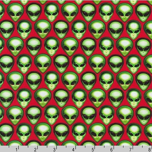 Red fabric with a repeating pattern of green alien heads, shown flat with a ruler at the bottom indicating scale.