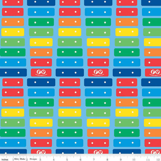 A repeating fabric pattern featuring colorful rectangular blocks in red, orange, yellow, green, and blue with small white dots, shown on a light blue background with a ruler along the bottom edge.