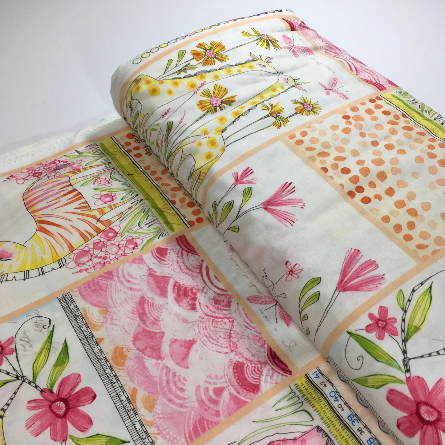 A folded and rolled fabric bolt, featuring a patchwork design of various watercolor floral , animals and geometric patterns in pink, orange, yellow, and green on a white background.
