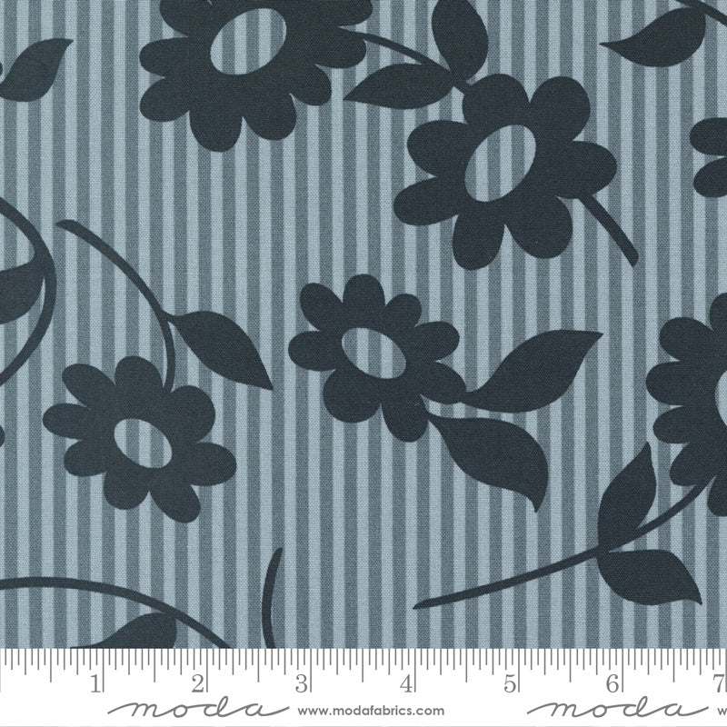 A close-up of fabric showing a repeating floral pattern with dark navy flower silhouettes and leaves over a muted blue-gray and navy vertical stripe background. A ruler along the bottom edge shows the scale.