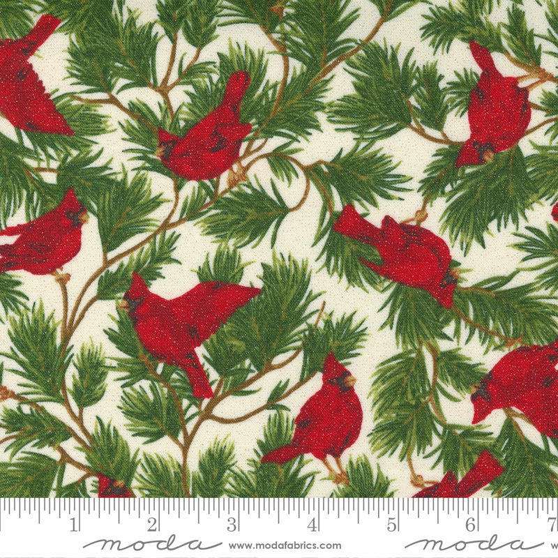 A close-up of a fabric pattern featuring red cardinals perched on green pine branches over an off-white background, with a ruler along the bottom edge showing scale. The brand name 'Moda' is printed at the bottom.