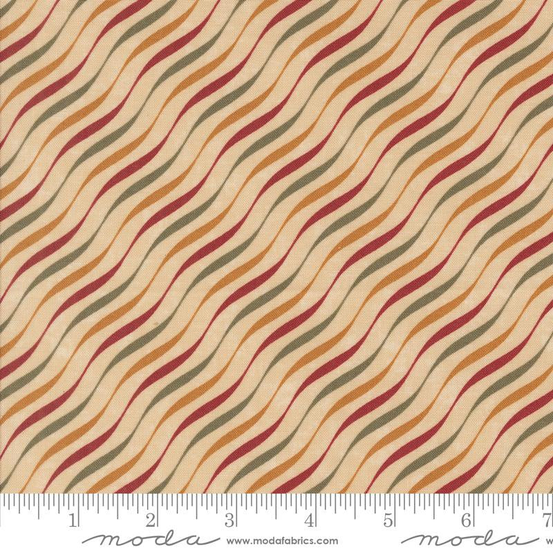 A close-up of a fabric pattern with wavy diagonal stripes in rust red, mustard yellow, olive green, and dark brown on a warm beige background, with a Moda brand inches ruler along the bottom edge.