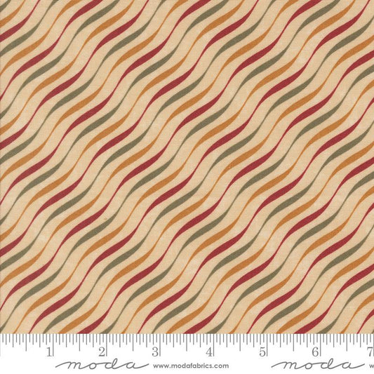 A close-up of a fabric pattern with wavy diagonal stripes in rust red, mustard yellow, olive green, and dark brown on a warm beige background, with a Moda brand inches ruler along the bottom edge.