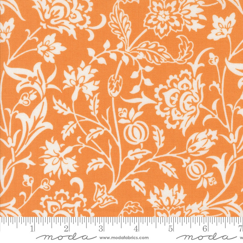 A close-up of a fabric pattern featuring a white floral and botanical print on a bright orange background, with a white ruler along the bottom edge showing scale. The brand name 'moda fabrics' is printed at the bottom.