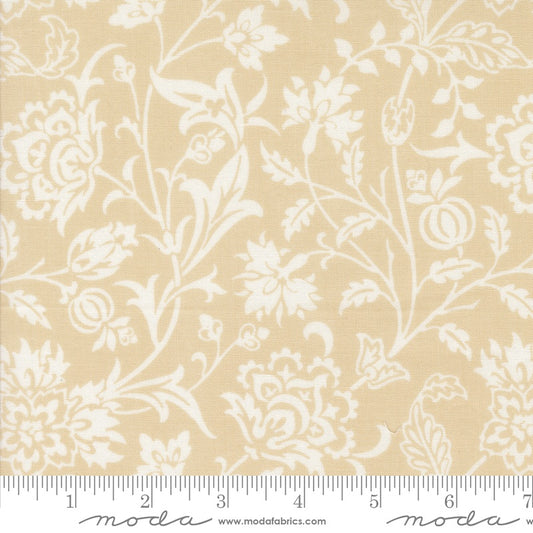 A close-up of a fabric pattern showing a cream floral and botanical scroll design on a warm beige background, with a white ruler printed along the bottom edge for scale. The brand name 'Moda' is visible at the bottom.