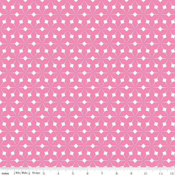 Pink and white geometric patterned fabric with a repeating starburst motif, shown flat with a ruler along the bottom edge for scale.