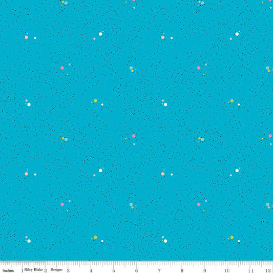 A repeating fabric pattern on a bright turquoise blue background with tiny scattered dots and small floral motifs in pink, yellow, green, and white. A white ruler along the bottom edge shows measurements in inches and includes the text 'Riley Blake Designs'.
