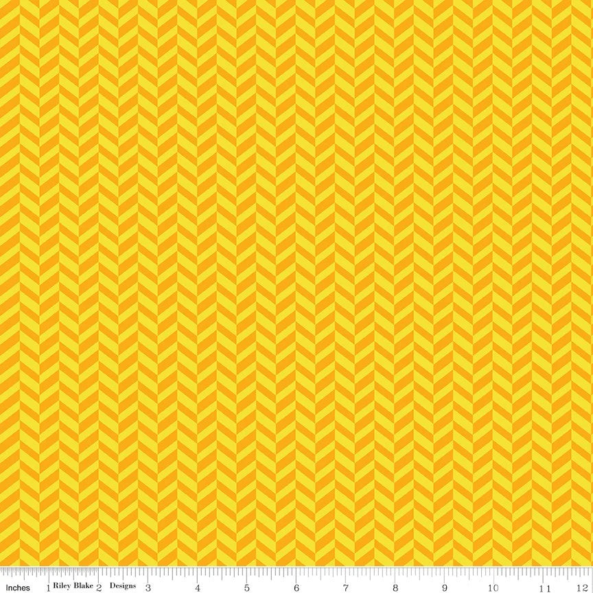 A close-up of a fabric pattern featuring a repeating yellow and orange chevron design, with a measuring ruler visible along the bottom edge.