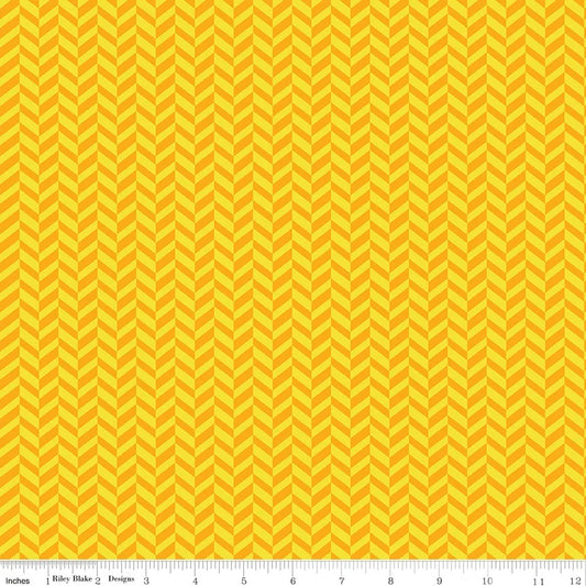 A close-up of a fabric pattern featuring a repeating yellow and orange chevron design, with a measuring ruler visible along the bottom edge.