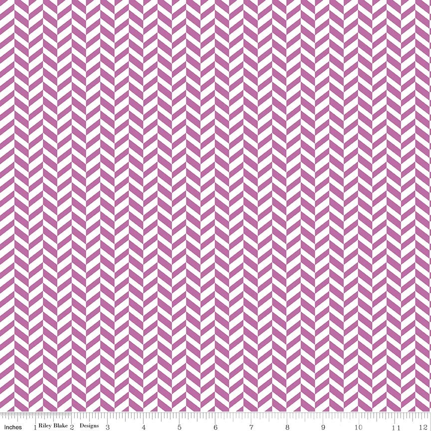 A close-up of fabric with a repeating purple pink and white chevron pattern, shown with a ruler along the bottom edge for scale.