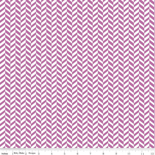 A close-up of fabric with a repeating purple pink and white chevron pattern, shown with a ruler along the bottom edge for scale.
