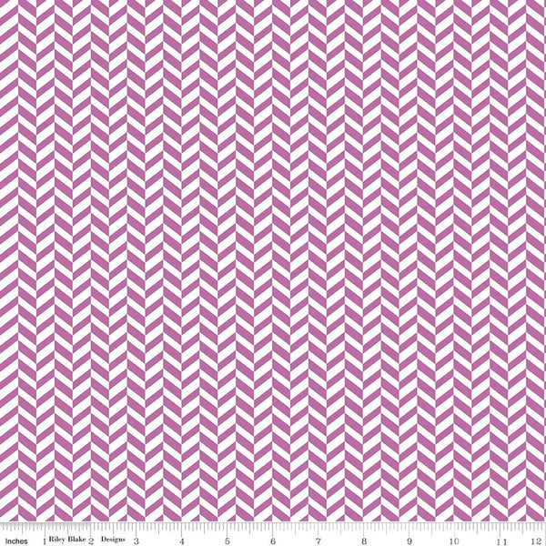 A close-up of fabric with a repeating purple pink and white chevron pattern, shown with a ruler along the bottom edge for scale.