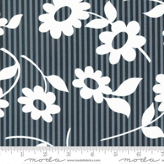 A close-up of a fabric pattern featuring white daisy flowers and leaves over a navy and gray vertical stripe background, with a measuring ruler along the bottom edge showing scale.