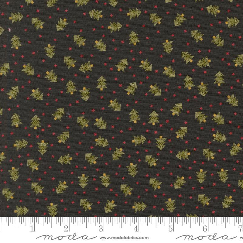 Black fabric with a repeating pattern of small gold Christmas trees and red dots, shown flat with a white ruler along the bottom edge for scale. The word 'moda' and website text appear at the bottom.