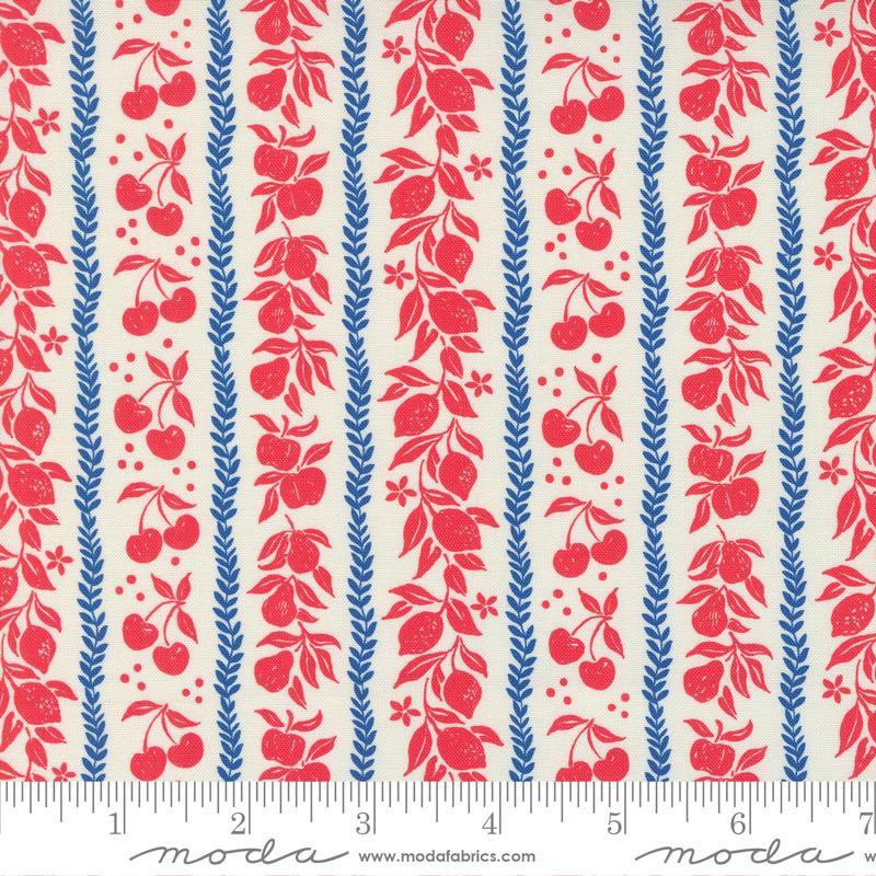 A close-up of a fabric pattern featuring vertical columns of red fruit motifs (cherries, peaches, strawberries) and blue leafy stalks on a warm cream background, with a ruler along the bottom edge showing scale.