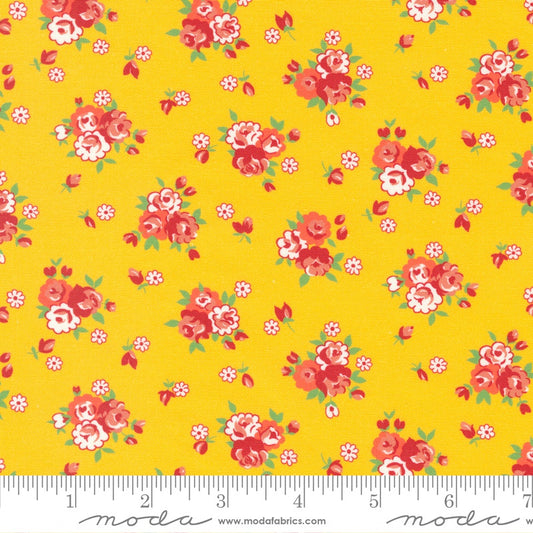 Yellow fabric with a repeating floral pattern of red, pink, and white roses with green leaves, shown with a measuring ruler along the bottom edge.