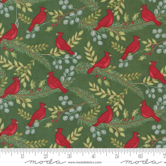 A close-up of a fabric pattern featuring red cardinals perched on green pine branches with small red berries and pale gray berries, shown with a measuring ruler along the bottom edge and the Moda brand name visible.