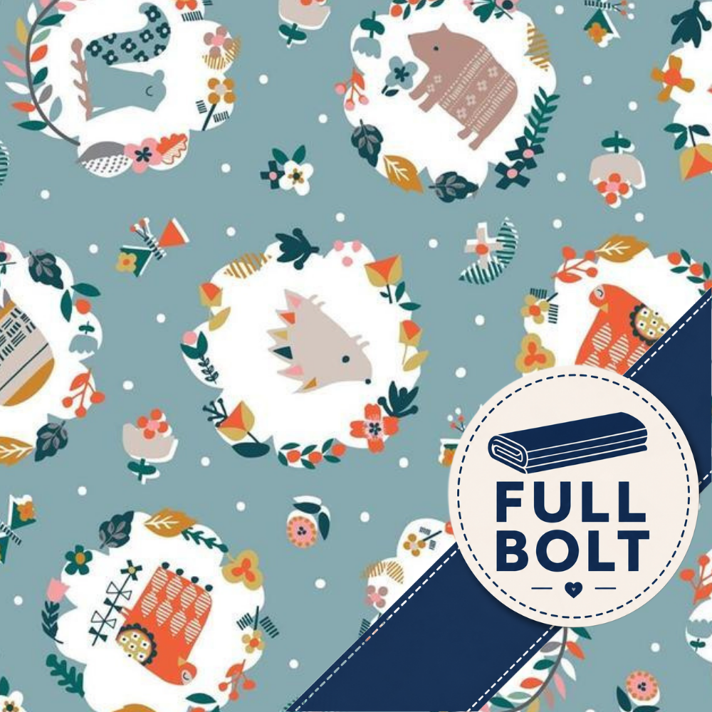A repeating fabric pattern on a muted blue-gray background, featuring whimsical woodland animal illustrations inside white oval frames, small floral wreaths, and a dark blue diagonal band with a circular badge reading FULL BOLT.