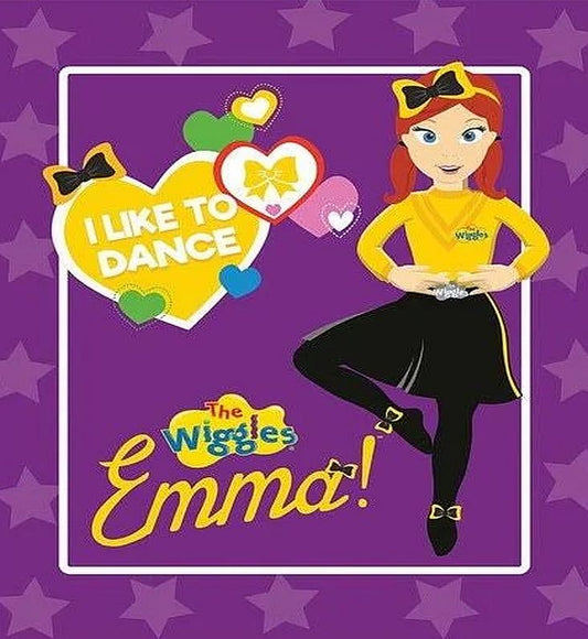 The Wiggles Emma fabric panel featuring a cartoon illustration of Emma in her signature yellow top and black skirt against a purple star background, with the text 'I LIKE TO DANCE' and 'The Wiggles Emma!'.