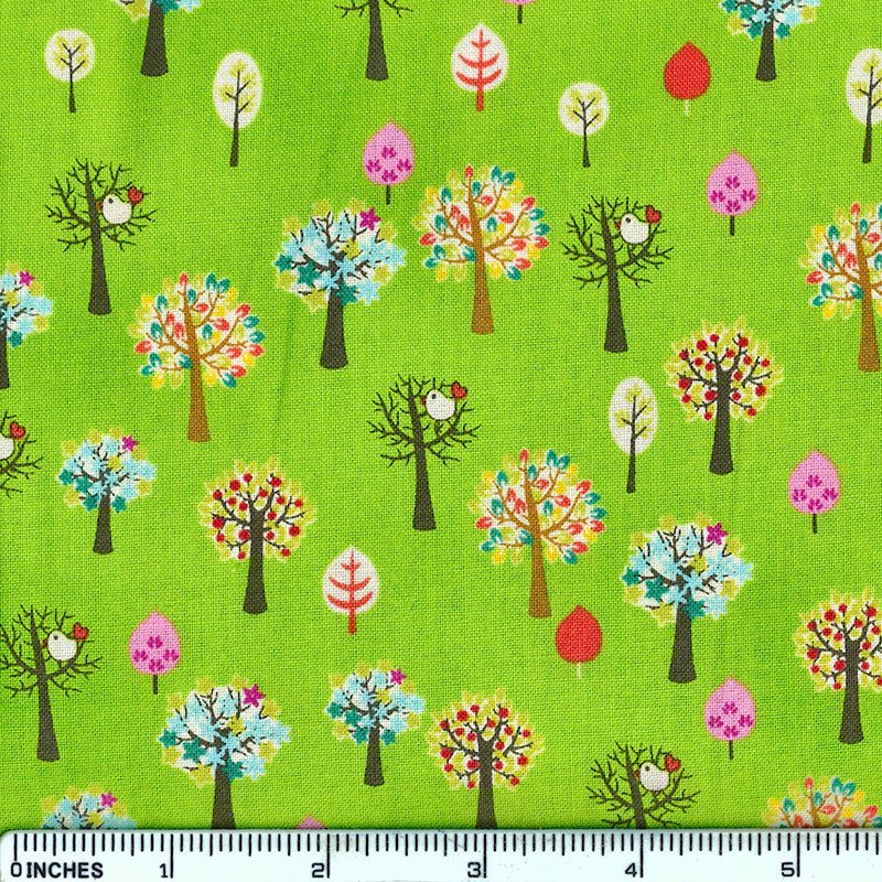 Bright green fabric with a repeating pattern of stylized trees in multiple colors, including pink, red, blue, yellow, and white, with a 12-inch ruler along the bottom edge for scale.