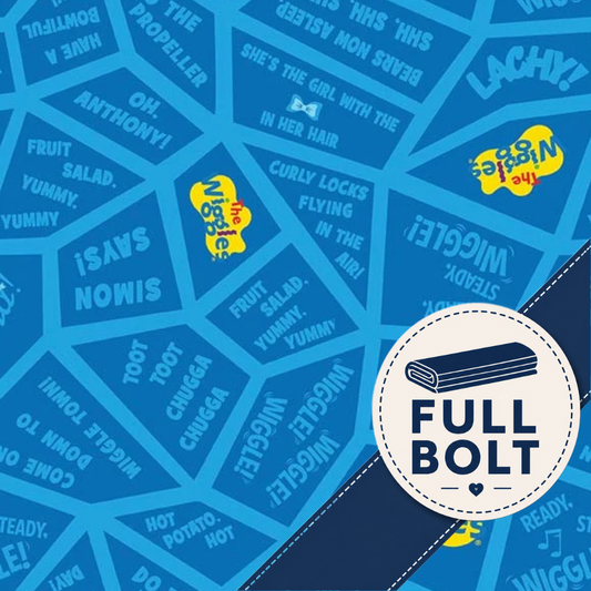Blue patterned fabric featuring repeated white text phrases and yellow 'The Wiggle' logo patches, with a large white circular badge reading 'FULL BOLT' and a dark navy diagonal band across the lower right.